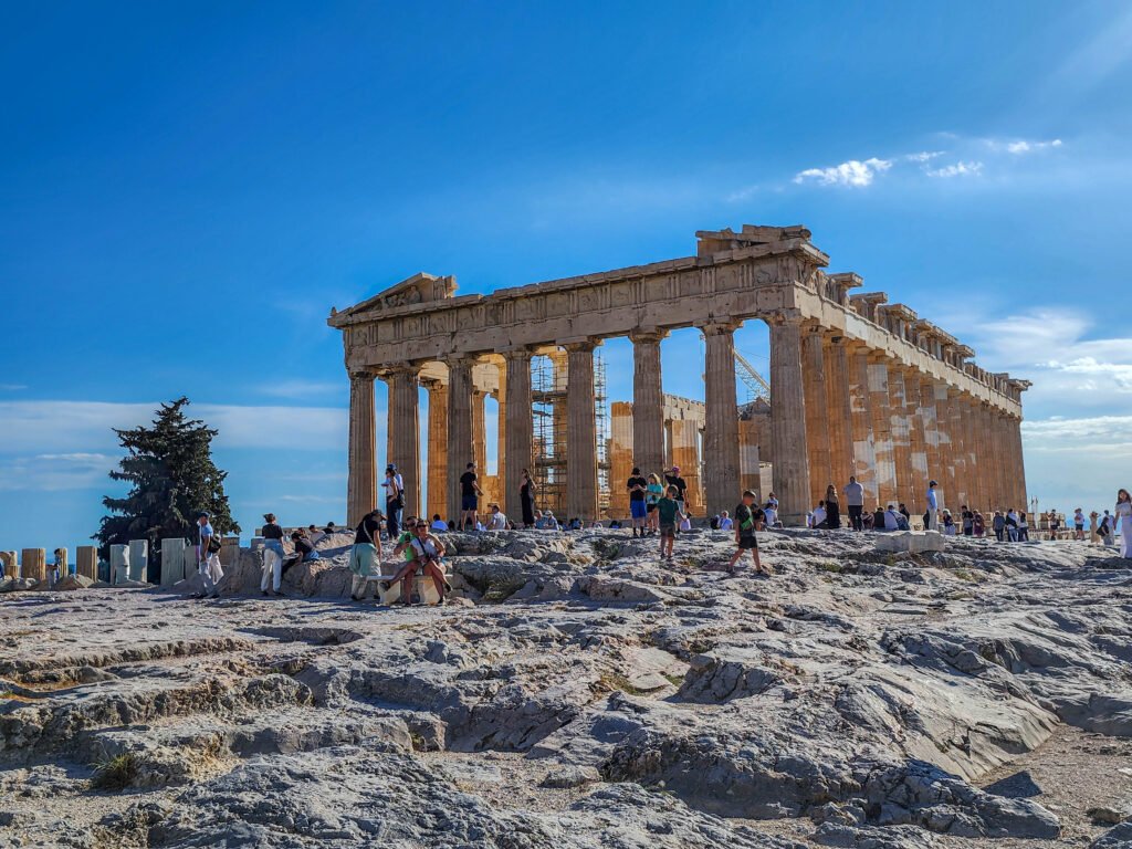 The Parthenon on the Acropolis Hill, slow travel Athens Greece — visitors exploring the ancient marble site under a clear blue sky