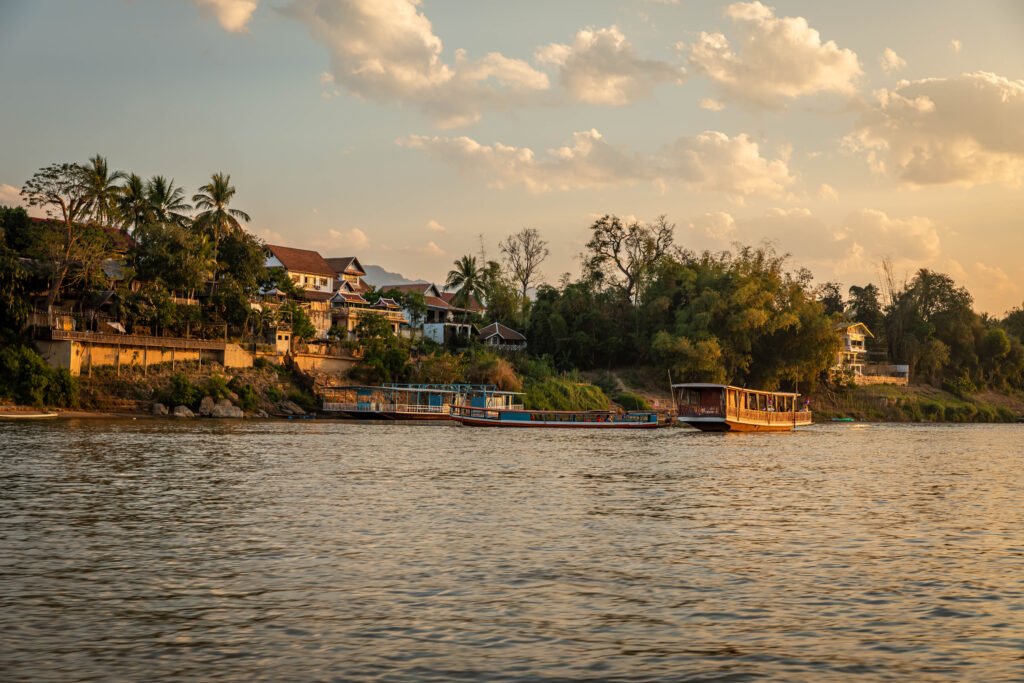 Traditional Lao houses and wooden boats on the Mekong riverbank at golden hour, Luang Prabang slow travel Laos