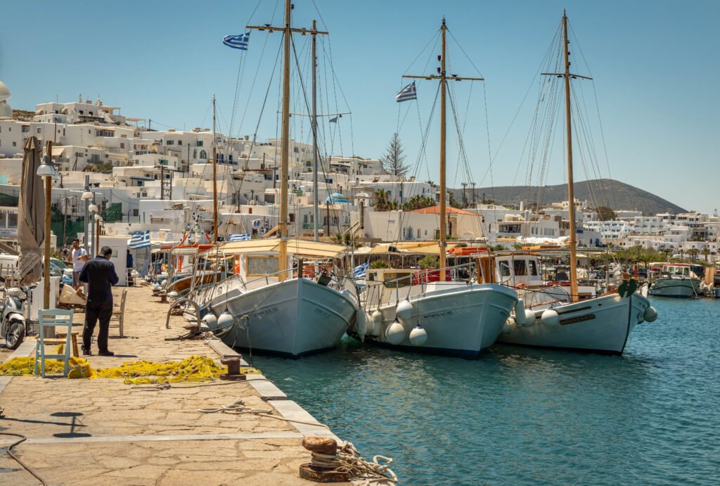 Fishing boats moored at Naousa harbour, slow travel Paros Greece — whitewashed Cycladic village rising behind the waterfront