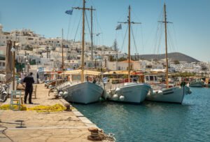**Alt text:** `Fishing boats moored at Naousa harbour, slow travel Paros Greece — whitewashed Cycladic village rising behind the waterfront`