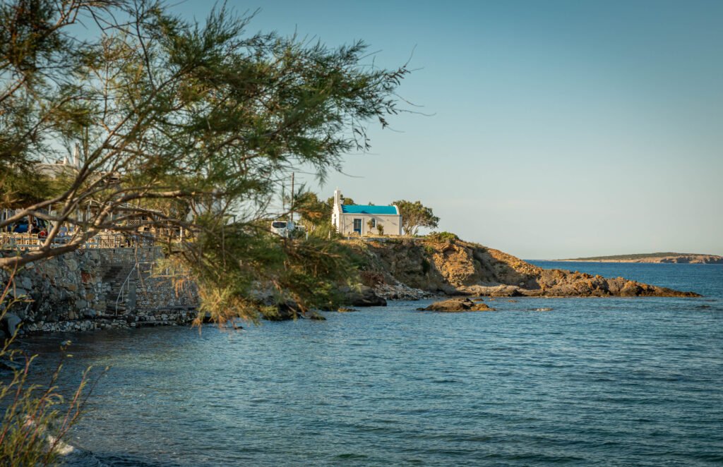 White chapel with blue roof on a rocky headland in Ampelas, slow travel Paros Greece — Aegean Sea at golden hour