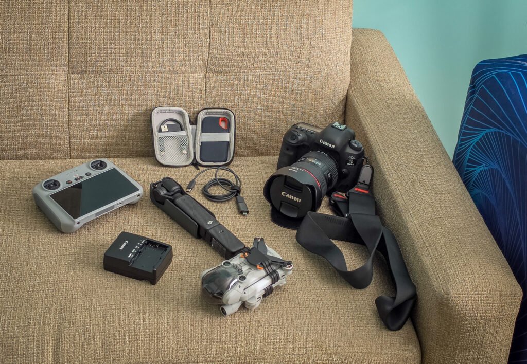 Slow travel packing essentials — Canon EOS 5D Mark IV camera, DJI Osmo Pocket 3, drone and remote controller, portable SSD, and charging cables