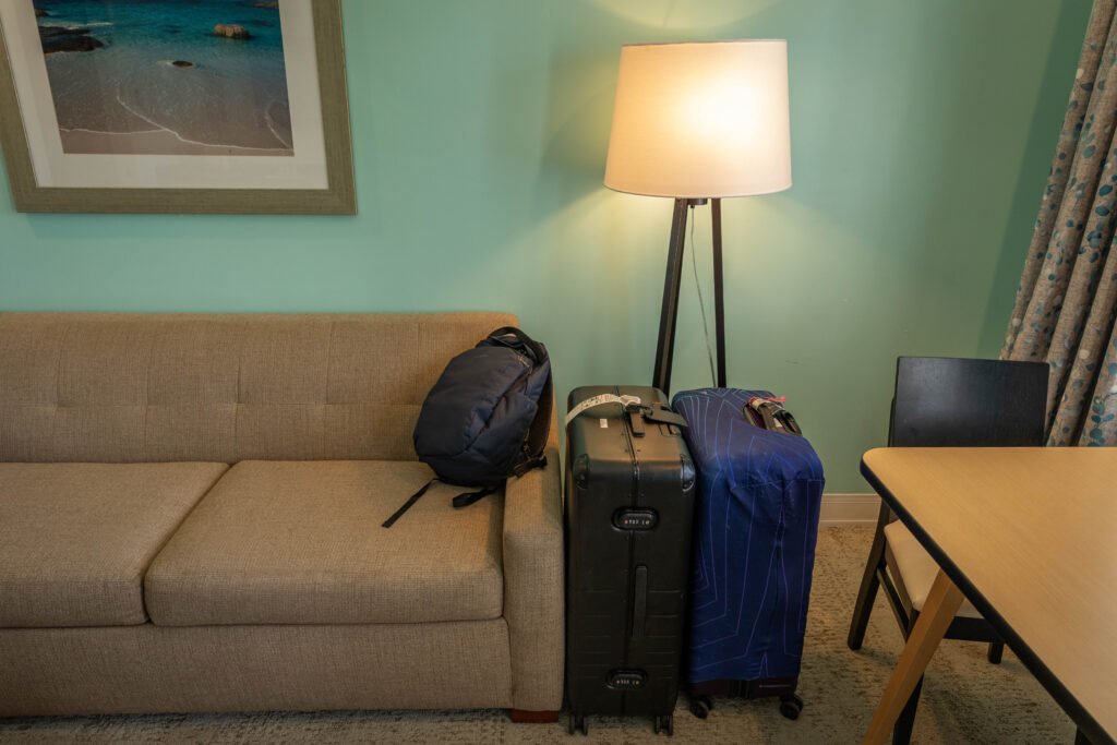 Two checked bags, a backpack, and a luggage cover packed and ready by the door in a hotel room
